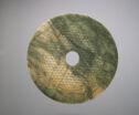 A dark green jade disk with a circle cut out in the middle. The center circle is fairly small. There is a faint pattern throughout the piece made of small circles.