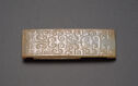 A jade buckle piece that is shaped into a rectangle and shown horizontally. It is pale yellow-green in color. There are many swirling relief lines through the piece that create a pattern.