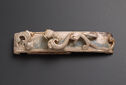 Long rectangular buckle, slightly bowed, featuring two dragon-like animals in relief slinking across the object, eyes locked on each other.