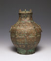 A brown cast bronze vessel with gold and turquoise inlay. The body is round with a small neck and flat lid. The left and right have small rings attached. The entire piece is inscribed with a detailed geometric, swirling pattern. 