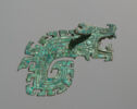 A blue-green bronze sculpture of a dragon-like form that is covered in inlaid turquoise pieces. It is flat. The head of the dragon has its mouth open, its ears point outward, and its body is a thick line that curls inward with geometric shapes along the outer edge.