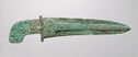 A blue-green bronze blade that is long with a short, curved handle. A thick line runs through the center of the blade that has small turquoise inlaid pieces. The round end of the handle also has turquoise inlaid pieces.