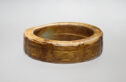 A jade ring that is caramel colored. It has an average-sized band width. There are relief-cut shapes that create mask designs all around the piece.