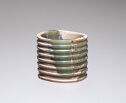 A jade ring that is green and off-white in color. The ring is tall and cut with many small horizontal ridges going down along the side of the piece.
