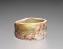 A jade bracelet that is pale yellow in color with some white and brown discoloration. It is a wide band and has engraved lines along its side. The top of the bracelet slopes down a bit.
