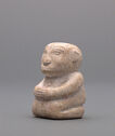 A jade figure of a stout, round man kneeling and sitting upright and facing the left. His hands are placed on his lap and his head is large and round. There are engraved lines on the figure to show fingers and details of the face. He is off-white in color