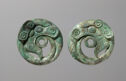 Two green cast bronze disks that have a small open circle in their centers. There is a swirling pattern around the center and fine engraved lines.