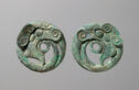 Two green/grey cast bronze disks that have a small open circle in their centers. There is a swirling pattern around the center and fine engraved lines.