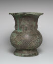 A green-grey cast bronze vessel that stands on a wide foot, has a round body, and a tall, flared out neck. It is decorated with engraved patterns that have fine lines, thick geometric lines, and an arched engraving along the top.