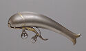 A grey steel object that is long and narrow in shape and curves down. The left end is wider and rounded while the right end is small and flares out in two ends. A long, thin piece curves underneath the object and has gold detailing.