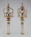 Two objects which look like chandeliers of bells which stand on cylindrical handles.