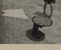 A black and white photograph of a person, an article of clothing, and a round dish on a stand.