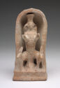 A terracotta sculpture of an abstracted figure standing under an arched form. Two animal heads with long antlers are on each side of the figure.
