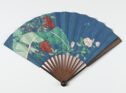 A dark blue fold-out fan with large leaves, red berries, and pink flowers painted on it. There are two small flying bugs painted on it as well and the handle is inscribed.