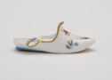 A delicate women’s slipper stands alone; it’s painted with small sprigs of blue and red flowers with green leaves.
