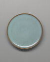 A circular dish shown from above. It is flat and colored pale blue with a thin, tan rim.
