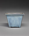 A square-shaped ceramic vessel with tall, straight walls. The top lip is flat and the feet are very small. It is colored light blue throughout.