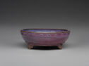 A low, wide purple ceramic basin with small pointed feet and a band with small, tan circles widely spaced out along the top lip.