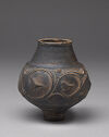 Black and brown-colored beaker with small round base, wide mouth, and wider spherical middle with vine and leaf raised designs 