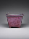 A square-shaped ceramic vessel with tall, straight walls. The top lip is flat and the feet are very small. It is colored magenta on the outside and faded blue on the inside.