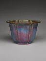 An aqua and magenta ceramic flower pot with vertical lines widely spaced out on the side. The flat, thin top rim protrudes out. The rim curves to mimic large petals. The inside is blue.