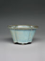 A light blue stoneware vessel with high walls, a flat jutted out lip, and indented lines along the outside.