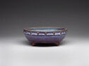 A low, wide blue and purple ceramic basin with small pointed feet and a band with small, tan circles widely spaced out along the top lip. The inside is blue.