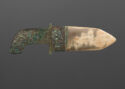 A polished jade blade is set in a bronze handle inlaid with turquoise