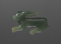 A profile view of a jade sculpture of a rabbit. The rabbit’s head faces the left side and its ears are straight back. Its front and back legs are straight out beneath its body and pointing forward.