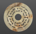 An off-white jade disk with a circle cut out in the middle. There is an outer ring that has a pattern of small circles. The inner ring has many curved forms with their negative spaces cut out.