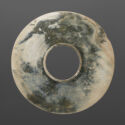A dark green and white jade disk with a circle cut out in the middle. There are many carved rings on the piece.