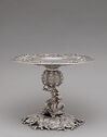 A silver platter raised on a decorative pedestal. 