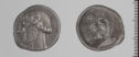 Both sides of an irregularly shaped silver gray coin with relief decoration on each side.     