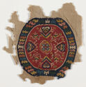 A textile fragment showing a roundel with a red center and a dark blue border. The border contains horizontal stripes of various colors and the roundel has a multicolored pattern of hearts, flowers, and vines. 