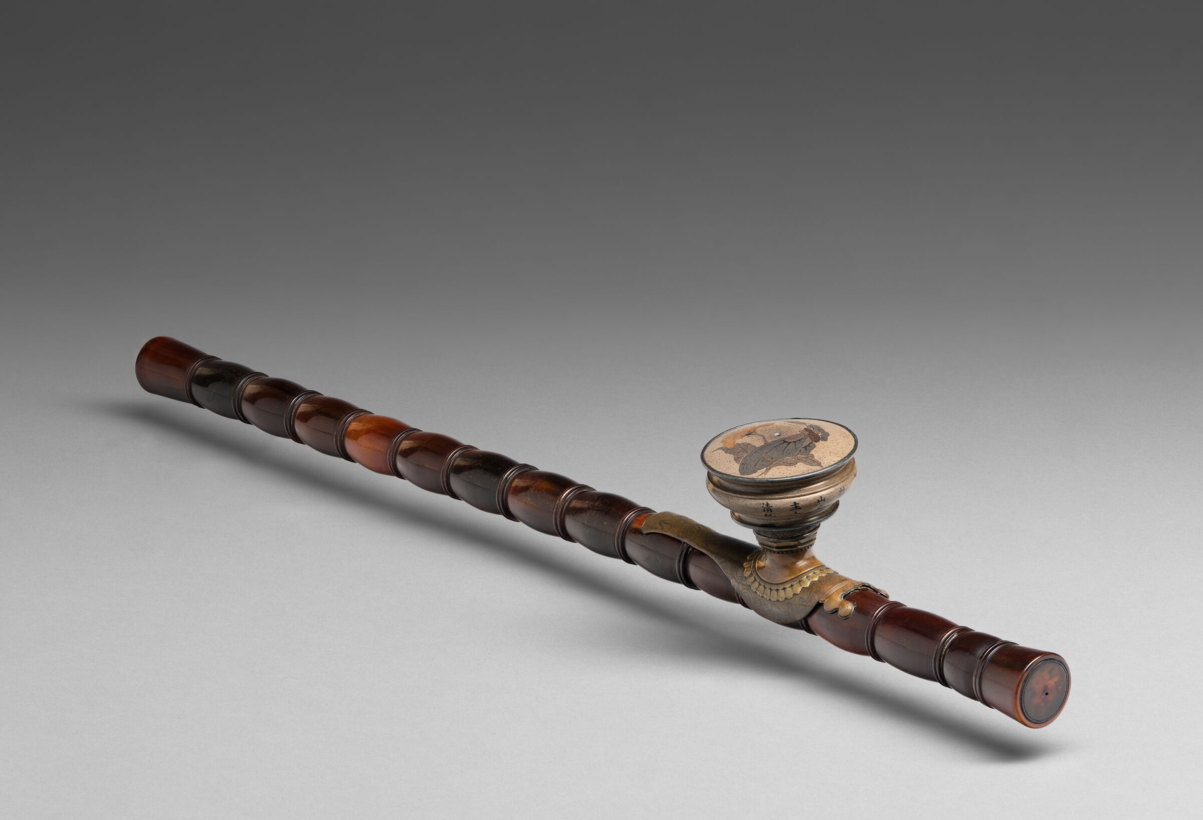 A brown opium pipe features a ceramic bowl decorated with a butterfly and poppy flowers.