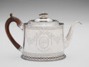 Silver teapot with engraved designed on the front, wooden handle, spout points to the right.