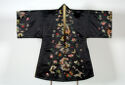 A wide satin coat hung with its sleeves straight out. The coat is black with a sheen. Along the edges of the sleeves and front opening is a spaced out pattern of colorful butterflies, flowers, and greenery.
