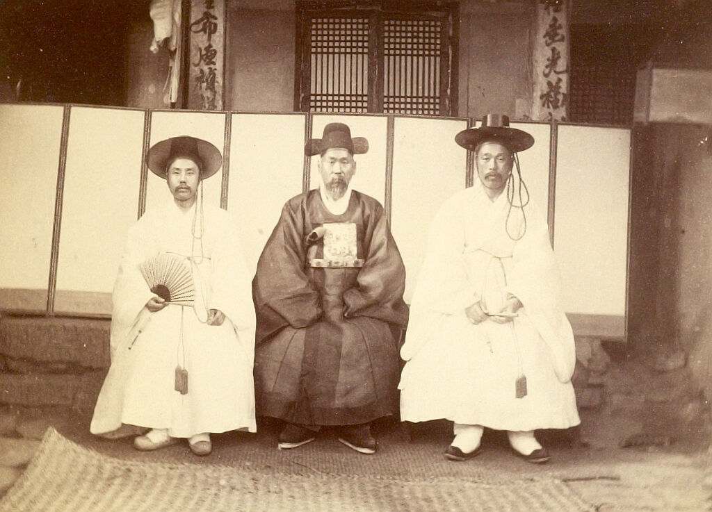 Three Korean Gentlemen Seated On The Veranda Of A House (Or Official Building)
