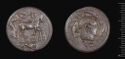 Both sides of an irregularly shaped silver gray coin with relief decoration on each side.    