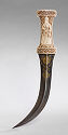 A curved, black blade with an ivory handle. The blade has gold curved decoration and the handle has carved details of Arabic script and the figure of a standing man.