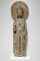 A limestone sculpture of a figure standing upright and wearing a decorated robe that covers their arms and goes to their feet. They are wearing a crown and there is a faded red circle behind their head. Their right hand has been broken off.