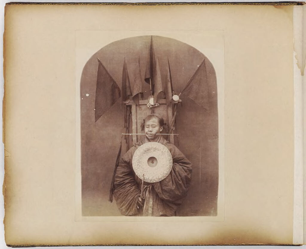 Untitled (Man With Pointed Stick Through Left Cheek, Holding A Metal Disk)