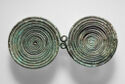 A pair of metal disks, each formed by coiling the thin metal into a spiral, are joined at their edge by two small loops.