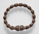 A ring of dark brown metal that does not close at the bottom, decorated with evenly spaced beads of the same metal.