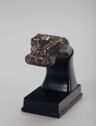 A black cast bronze animal head with gold decorations on the top. The head has a wide, flat snout, round eyes on both sides, and small ears on top on each side. The neck is attached to a black mount that comes to a flat rectangular bottom.