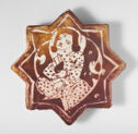 A flat, lusterware tile that is in the shape of an eight pointed star. It is brown and tan colored with white lines outlining a seated figure in the center.