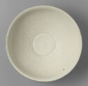 A ding ware circular bowl that has been engraved with loose, swirling lines that make a botanical design. It is off-white in color and the body is wide.