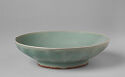 A green-blue ceramic dish that is wide and low. It has a wide, stout foot.  