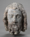 A gray stone head of a man with curly hair and a curly beard