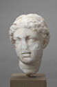 A white marble sculpture depicts the head of a youth with a broken nose atop a square stone display block.